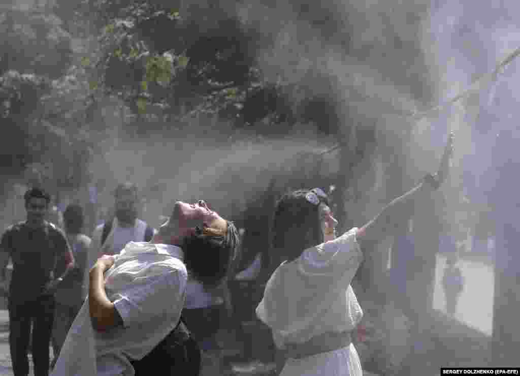 Ukrainians cool themselves with water sprayed from pipes hanging over a sidewalk during hot weather in central Kyiv.