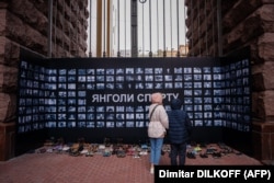 Жінки розглядають стіну з фотографіями двохсот українських спортсменів, які загинули внаслідок російського вторгнення в Україну, на виставці під назвою «Янголи спорту» в Києві, 18 квітня 2023 року