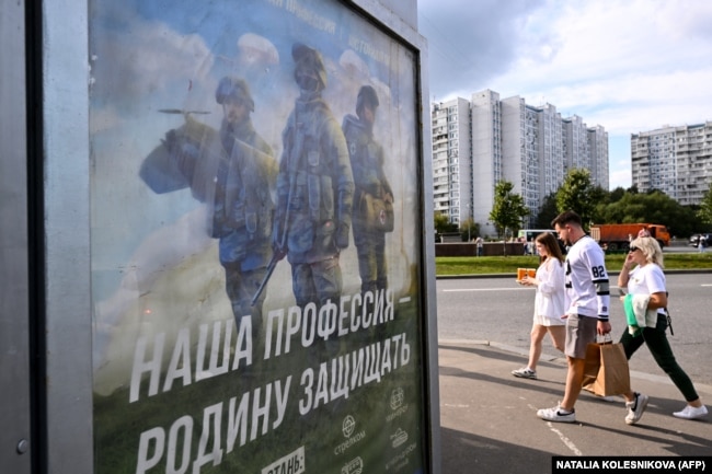 Люди проходять повз плакат з пропагуванням контрактної армії та написом «Наша робота – захист батьківщини»