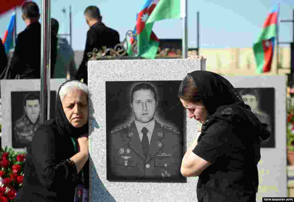 Relatives mourn next to a portrait on a tombstone at a memorial cemetery in Baku.