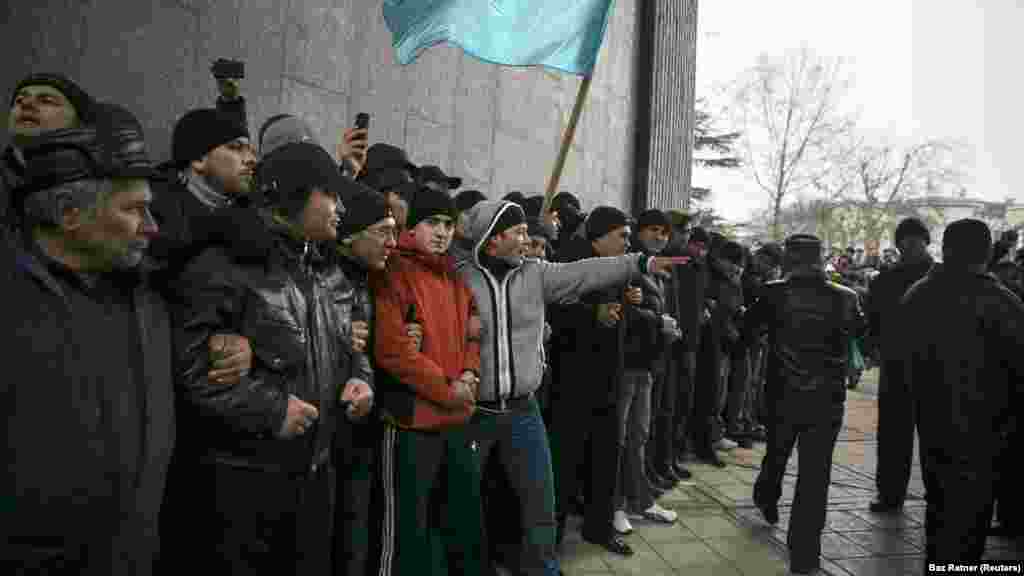 Krími tatárok a zászlójukkal a krími parlamentnél tartott tüntetésen Szimferopolban 2014. február 26-án. Egy héttel korábban egy krími politikus felvetette a félsziget Ukrajnától való elszakadásának lehetőségét. A kijevi tüntetők akkoriban éppen azon voltak, hogy kiszorítsák a hatalomból Viktor Janukovics oroszbarát elnököt, amit az ukránok &bdquo;a méltóság forradalmának&rdquo;&nbsp;neveztek el