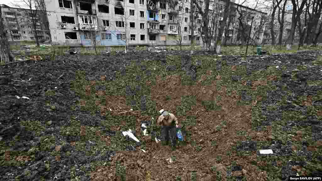 Un bărbat în vârstă cu vederea slabă se ridică după ce a căzut într-un crater de explozie în orașul Avdiivka de pe linia frontului, Ucraina.
