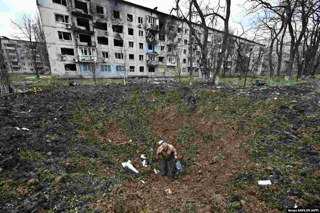 Un bărbat în vârstă cu vederea slabă se ridică după ce a căzut într-un crater de explozie în orașul Avdiivka de pe linia frontului, Ucraina.
