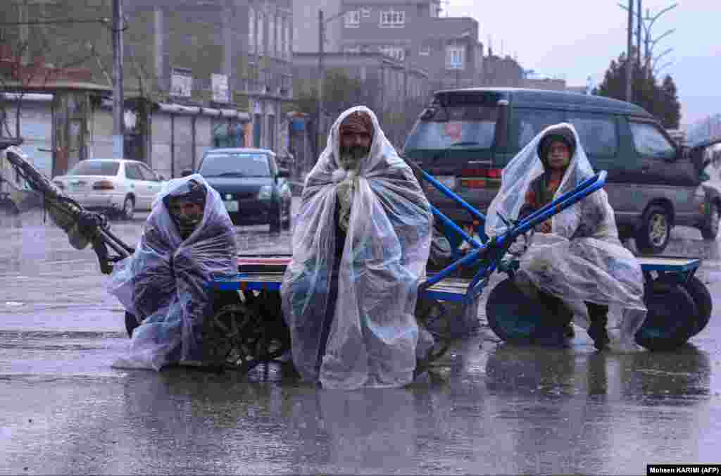  Afghan workers cover themselves with plastic sheets during heavy rainfall as they sit on their hand carts along a road in Herat. &nbsp; 