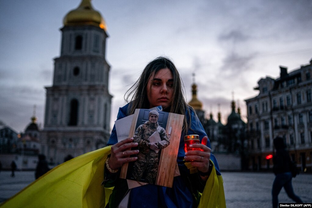 Një grua mban një qiri dhe një portret të burrit të saj, i cili u kap gjatë rrethimit të qytetit port të Mariupolit, gjatë një tubimi për të nderuar mbrojtësit e Ukrainës si pjesë e Ditës së Vullnetarit, në Kiev më 14 mars.