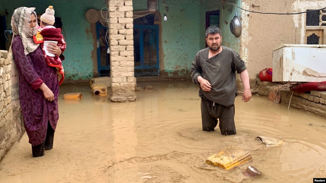 O mamă afgană își protejează copilul, iar un bărbat încearcă să mai salveze ceva din casa lor din Maymana, capitala provinciei Faryab din nordul Afganistanului (mai 2024).