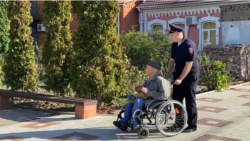 Сотрудник полиции катит инвалидную коляску с Юрием Трубачевым в суд 