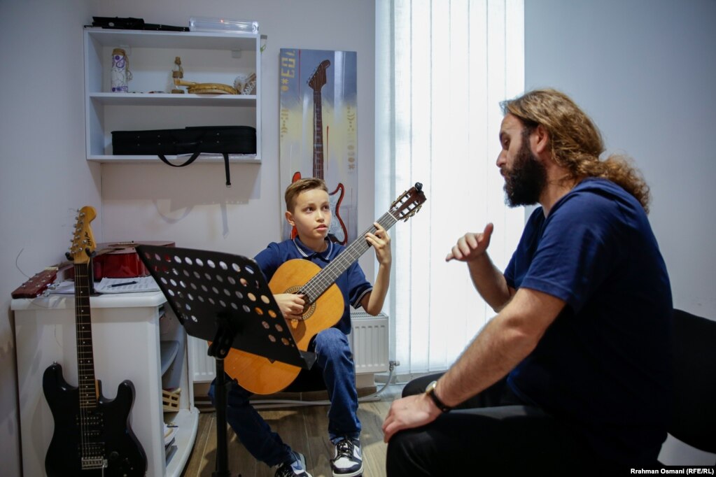 Ledion Halitaj duke mbajtur orën e kitarës me mësuesin e tij, Erhan Mujka.