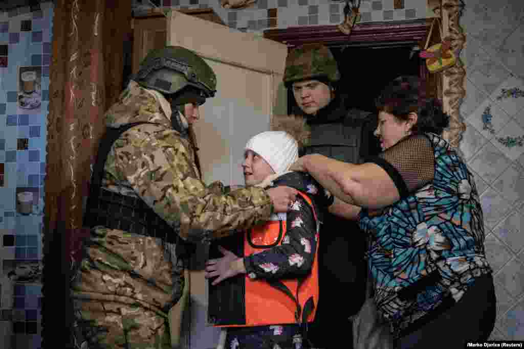 Valeria, a member of the White Angel unit of Ukrainian police officers who evacuates people from the front line, places body armor on Vika Savchenko, 8, during her evacuation from her village of Zarichne.