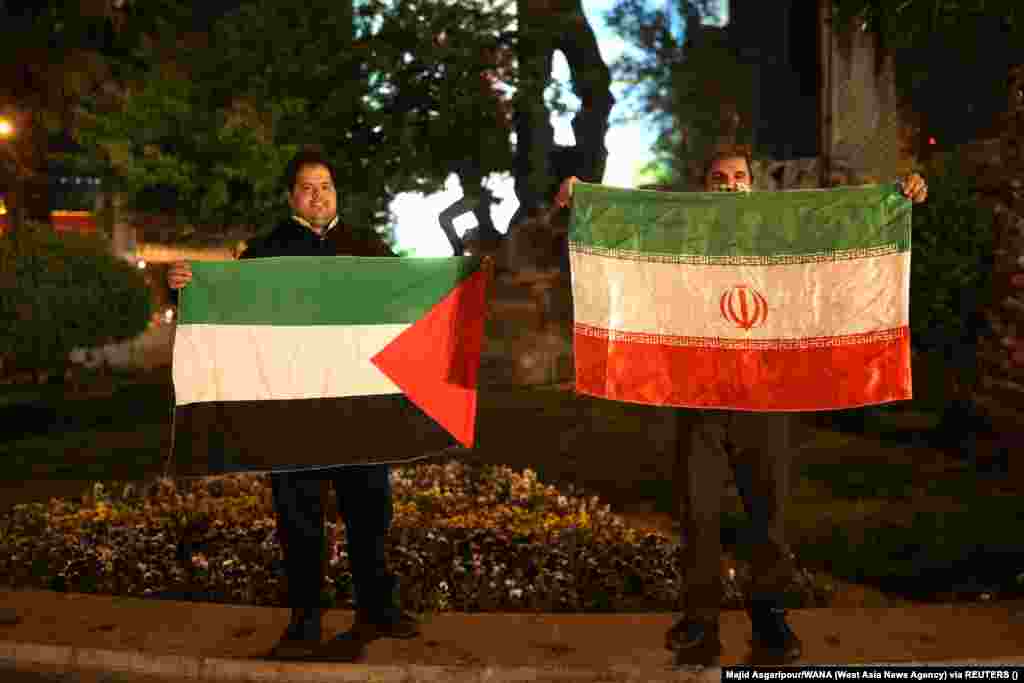 После массированной воздушной атаки на Израиль демонстранты в Тегеране держат флаги Палестины и Ирана
