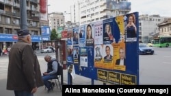 Panou cu afișe electorale în Piața Română. Un domn citește mesajele candidaților.