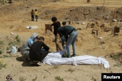 Palestinci pokrivaju tijelo, iskopano iz masovne grobnice, sjeverno područje Pojasa Gaze, 15. aprila 2024.