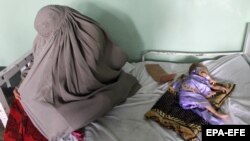 Owganystanyň Kandagar şäherinde syrkaw çagasynyň ýanynda oturan bir eje (arhiw suraty)