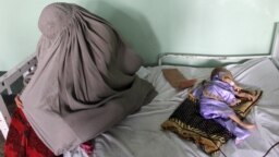 An Afghan woman sits next to a child suffering from malnutrition and other diseases while receiving treatment at Mirwais hospital in Kandahar.
