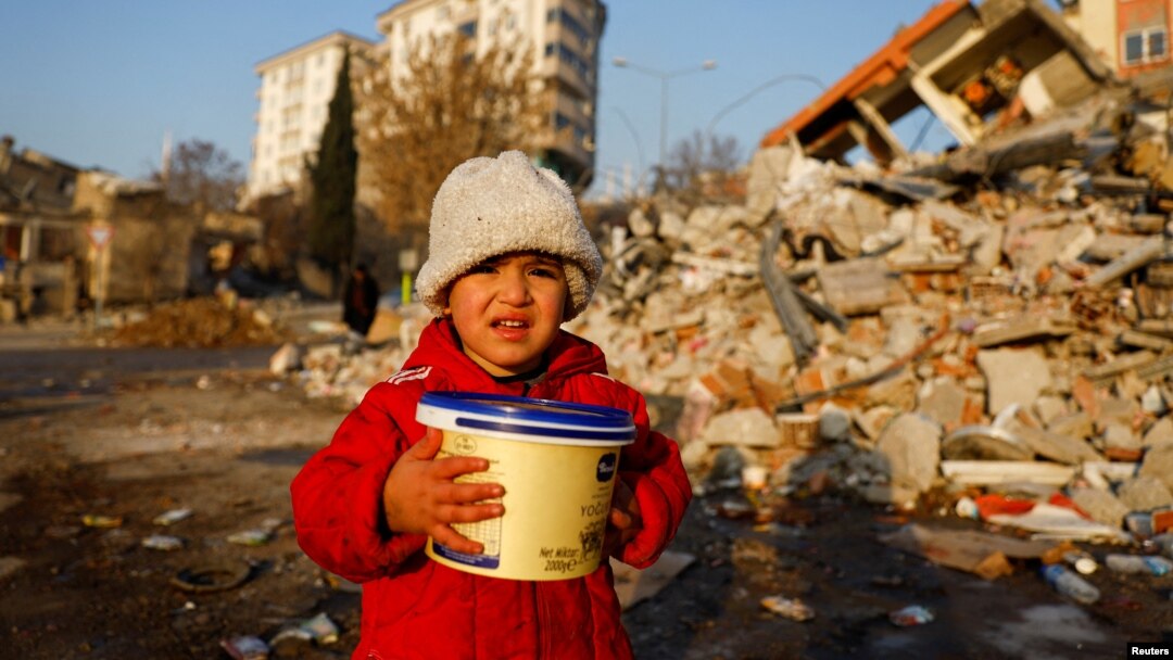 Un copil ține în mână o cutie de plastic printre dărâmături, în Kahramanmaraș, Turcia, 14 februarie 2023.