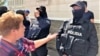 Женщина задаёт вопросы полицейскому у здания суда после вынесения приговора по делу о «захвате» алматинского аэропорта во время Январских событий. Алматы, 11 июля 2023 года