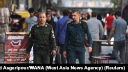 Two policemen walk through Tehran on July 16. The officer on the left is wearing the standard green uniform&nbsp;<strong><a href=https://www.rferl.org/a/iran-hijab-bill-parliament/