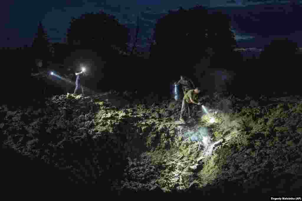 Ukrainian policemen search for rocket fragments in the large crater caused by the Russian missile attack.&nbsp;
