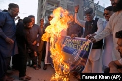 Активисты Объединенного мусульманского форума Пакистана сжигают изображение шведского флага во время демонстрации протеста против случаев осквернения Корана в Швеции. Карачи, 2 июля 2023 года