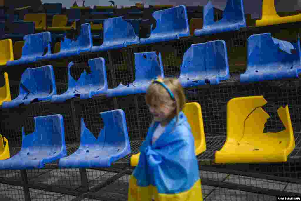 Дівчинка загорнута в прапор України стоїть перед пошкодженою військами РФ трибуною харківського стадіону &laquo;Сонячний&raquo;, яку виставили на площі в Мюнхені напередодні матчу збірної проти Румунії, Німеччина, 17 червня 2024 року
