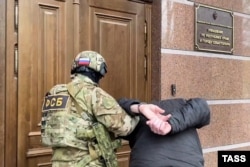 Сотрудник ФСБ сопровождает задержанного к зданию управления ФСБ в аннексированном Крыму, декабрь 2022 года