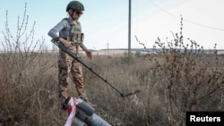 A member of the Demining of Ukraine NGO works near a piece of a MLRS shell in a field near the town of Derhachi in the eastern Kharkiv region. 