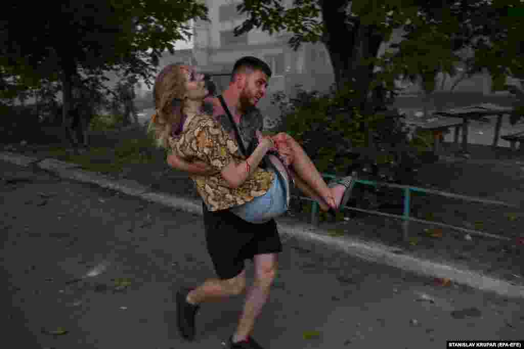 A man carries an injured woman after a second Russian missile struck an apartment building in the eastern Ukrainian city of Pokrovsk on August 7. The strikes, which occurred within 40 minutes of each other, damaged residential building, killing at least seven people -- two of whom were rescue workers -- and injuring dozens more.