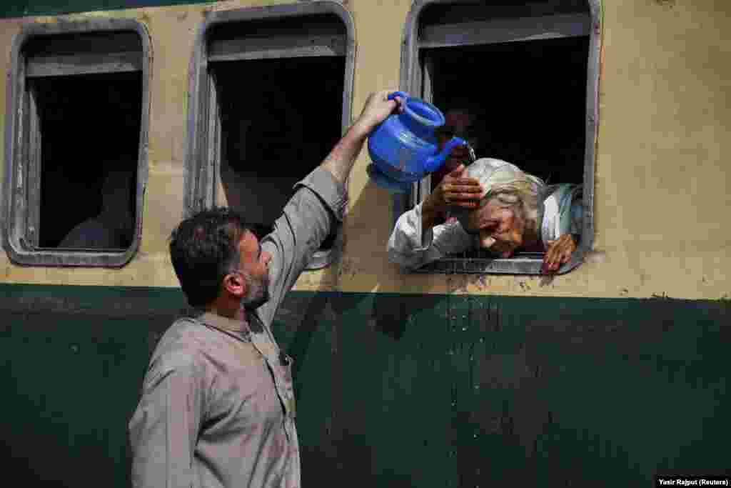 A woman, leaning out of a train window, receives water on her head to cool off during a hot and humid day at the Hyderabad Railway Station in Hyderabad, Pakistan.