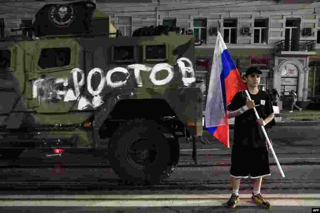 A man holds the Russian national flag in front of a Wagner vehicle with a painting that reads &quot;Rostov.&quot; &nbsp;