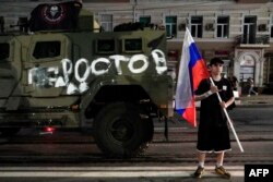 კაცს ხელში რუსეთის დროშა უჭირავს და „ვაგნერის“ სამხედრო მანქანის წინ დგას. ჯავშანმანქანაზე წარწერაა - "როსტოვი".
