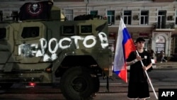 A man holds the Russian flag in front of a Wagner Group military vehicle painted with the word "Rostov" in Rostov-on-Don late on June 24.