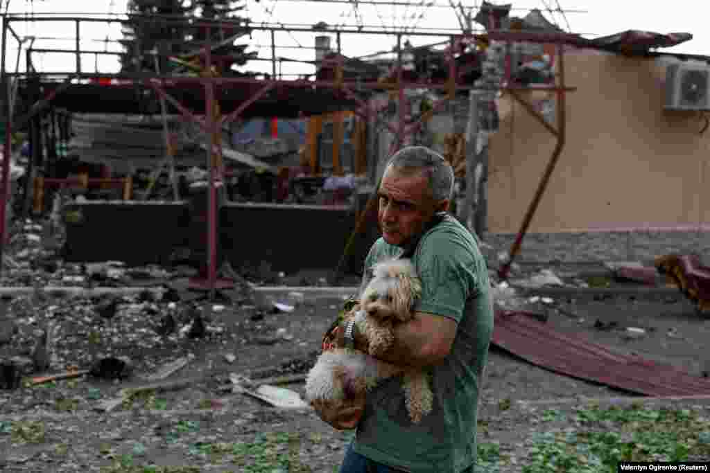 Një burrë mban një qen jashtë një kafeneje të shkatërruar që u godit nga një sulm ajror rus në qytetin verilindor të Ukrainës, Harkiv, më 22 maj.