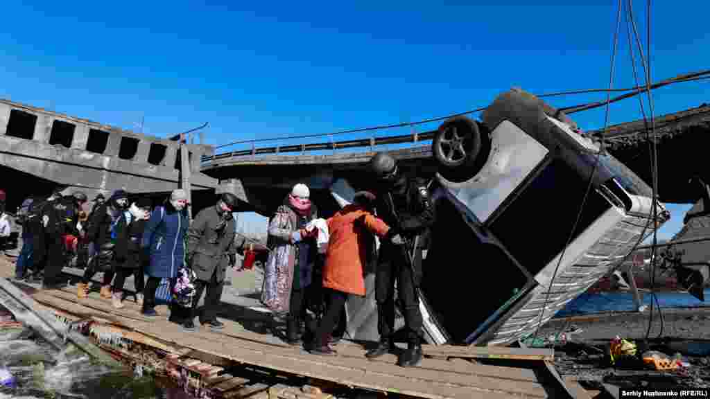A police officer helps civilians evacuate from Irpin under a destroyed bridge on March 12, 2022.