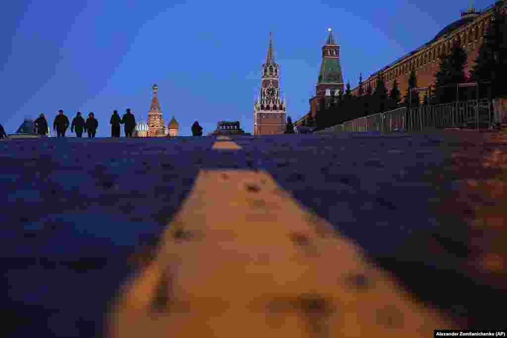 People walk in Red Square past St. Basil&#39;s Cathedral (left), Lenin&#39;s Mausoleum (center), the Spasskaya Tower, and the Kremlin Wall (right) after sunset in Moscow.