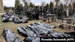 Полицейские рядом с телами погибших во время российской оккупации Бучи на местном кладбище, Киевская область. Украина, апрель 2022 года