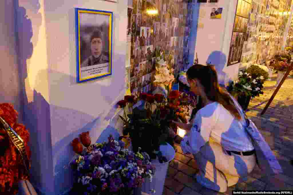 A woman places flowers next to a portrait of Andriy Babninskiy on the wall of Ukraine&#39;s fallen defenders.