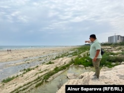 Активист Азамат Сарсенбаев показывает на отступившее от берега море. Актау, 16 июня 2023 года