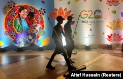 Прибиральники проходять повз рекламу в Міжнародному медіа-центрі під час саміту G20 у Нью-Делі, Індія, 9 вересня 2023 року