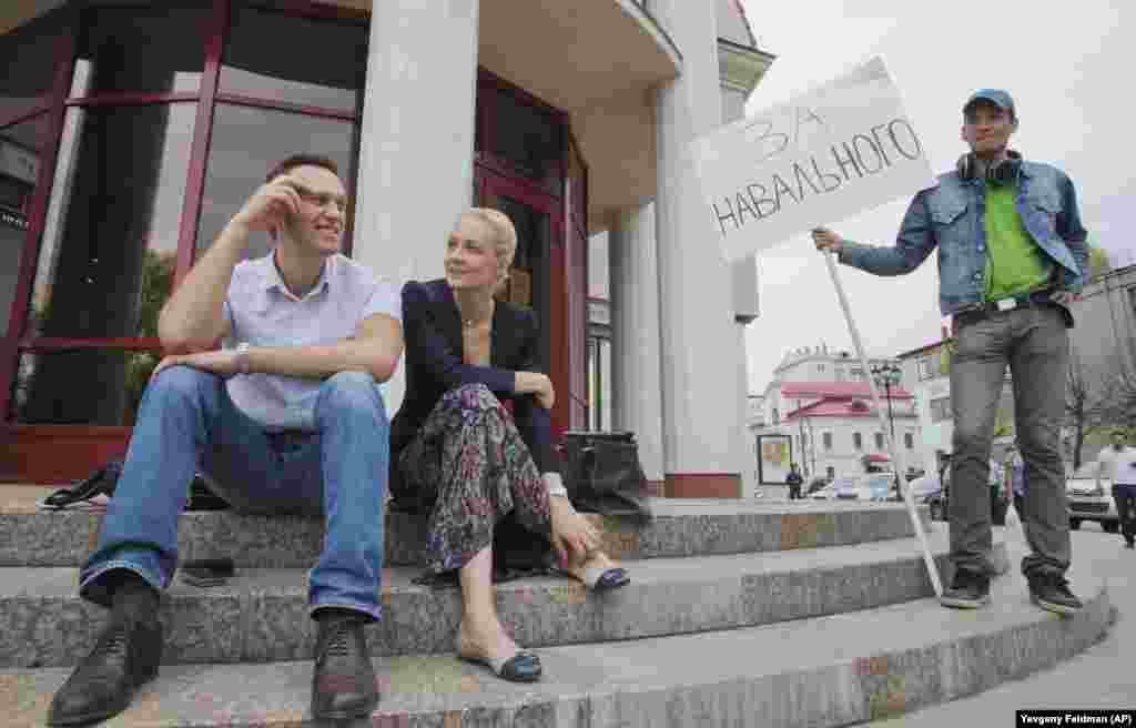 Navalny and his wife, Yulia, sit together after a court hearing as a supporter with a poster reading &quot;For Navalny&quot; looks on in the northwestern city of Kirov on May 16, 2013.&nbsp; Accused of embezzlement, Navalny insisted the charges were revenge for his exposure of high-level government corruption and for his campaigns against Putin.