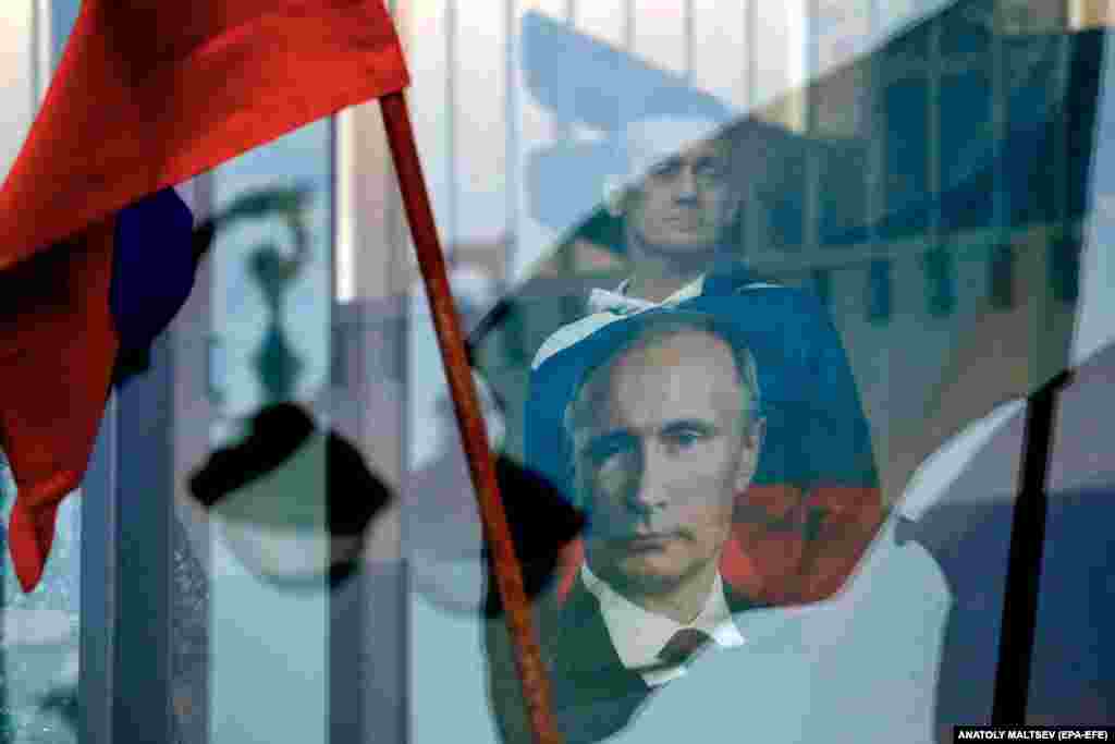 Čovek u majici s likom ruskog predsednika Vladimira Putina gleda kroz prozor dok policija čuva područje oko koncertne dvorane Oktjabrski u Sankt Peterburg.