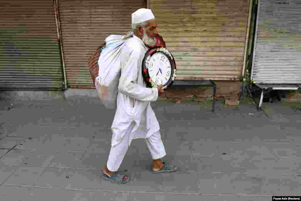 Një burrë që mban orë muri për shitje duke ecur përgjatë dyqaneve të mbyllura të këmbimit valutor në Peshavar, Pakistan.