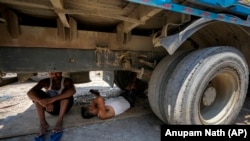 Radnici su od vrućine potražili utočište u senci ispod kamiona, Guvahati, 25. maj 2024.