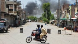 Men watch as smoke rises following an explosion after militants attacked an army base in Pakistan's northwestern city of Bannu on July 15.