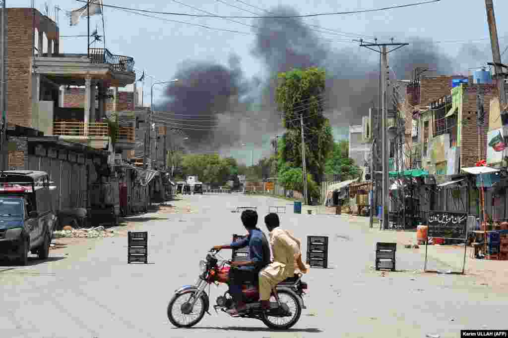 Dy burra në një motoçikletë duke shikuar tymin e zi që ngrihej pas një shpërthimi si rrjedhojë e një sulmi të kryer nga militantët ndaj një garnizoni ushtarak në Banu, Pakistan, më 15 korrik.