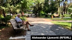 Pripadnik starije populacije sjedi na klupi u parku u Podgorici
