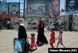 چند شهروند فلسطینی ساکن غزه، در حال عبور از مقابل تبلیغاتی فیلمی در مورد عماد عقل، نخستین فیلم سرمایه‌گذاری شده توسط حماس/ اواسط تابستان ۲۰۰۹