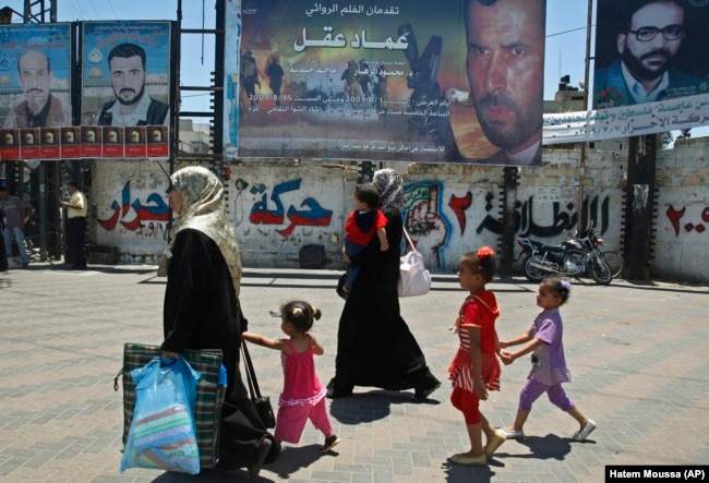 چند شهروند فلسطینی ساکن غزه، در حال عبور از مقابل تبلیغاتی فیلمی در مورد عماد عقل، نخستین فیلم سرمایه‌گذاری شده توسط حماس/ اواسط تابستان ۲۰۰۹