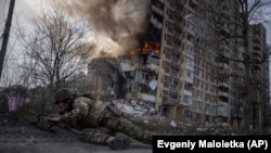 უკრაინელი ჯარისკაცი ალმოდებული შენობის ფონზე. ავდეევკა, უკრაინა. 2023 წლის 17 მარტი