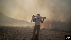 Un bărbat își acoperă fața cu un prosop în timp ce încearcă să stingă un incendiu în apropierea stațiunii balneare Lindos, pe insula Rodos din Marea Egee, în sud-estul Greciei, iulie 2023.