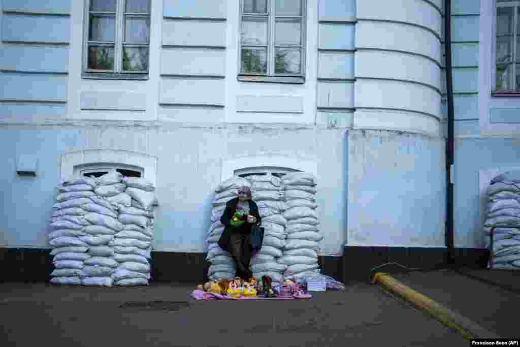 A woman sells toys in front of a building with windows protected by sandbags in Kyiv.